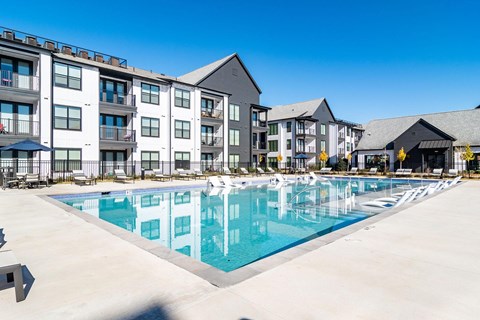 Dog-Friendly Apartments In Huntsville, AL - The Collins - Gated Resort-Style Salt Water Pool with Poolside and Submerged Lounge Seats, Tables, Chairs, Umbrellas, and View of Apartment Buildings